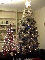 Two artificial trees lit up: a 5-foot flocked pre-lit tree with mixed white and blue lights and star topper and a 3-foot grapevine tree with multi-color lights.