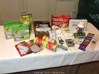 Box of various household essentials including socket sealers, batteries, health care items, and more on a white cloth surface.