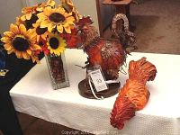 Photo showing metal rooster lamp, resin rooster figurine, cut glass vase with silk sunflowers arranged on table.
