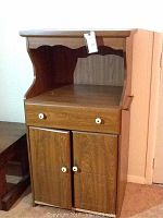 Front view of pressed wood microwave cart with upper open shelf, drawer, and double-door cabinet with white knobs.
