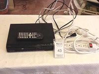Image showing Magnavox DVD player with remote on top, white surge protector, and HDMI cable on white towel surface.