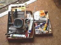Lot contents arranged on floor showing brushes, paint trays, rollers, tubes, and various tools in two cardboard boxes.