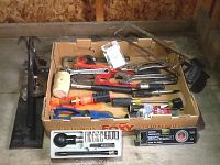 Multiple hand tools including screwdrivers, pliers, rubber mallet, hand saw, and assorted wrenches arranged in a box and on a concrete floor.