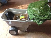 Heavy duty plastic garden cart with folded green leaf tarp inside and cardboard box containing assorted chemicals