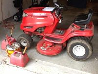 Side view of red Troy-Bilt Pony riding lawn tractor on garage floor with three red gas cans in front