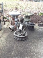 Photo showing two concrete Japanese garden lantern statues, meditating Buddha water fountain, and metal pagoda lanterns arranged on a patio.