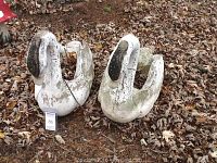 Pair of concrete swan planters placed on ground covered with dry leaves, showing condition and size relative to surroundings.