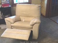 Front view of beige leather recliner with footrest extended, showing overall condition and visible scratch on right arm.