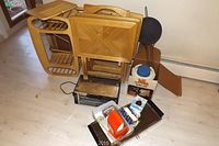 Photo showing three wooden folding tables, Proctor Sylex toaster oven, Aladdin Pump A Drink jug in box, heated tray, and cast iron pan