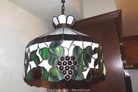 Full view of Tiffany style pendant lamp hanging, showing the stained glass lampshade with grape and leaf design and bronze tone chain.