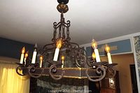 Side view of the rectangular wrought iron chandelier showing 10 candle-style bulbs, scrolled iron details, and bronze clasp accents along the frame, hanging from chain.