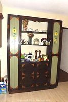 Front view of tall wooden pantry cabinet showing hand-painted side doors with sunflower designs and open shelves with decorative items.