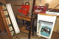 Workbench with metal legs, box on top, and nearby white cabinet with various items