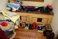 Wide view of the collection on bench and floor showing scarves, gloves, several pairs of shoes in boxes and on bench, blankets on left.