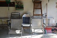 Photo of two folding metal mesh chairs, one white plastic chair with cushion, vintage wooden ladder, and garden tools in background