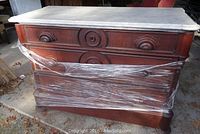 Front view of the vintage dresser showing white marble top and three drawers with cup-shaped pulls wrapped partially in plastic wrap.