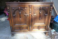 Front view of the vintage solid wood dresser showing two carved wood doors with molded panels and carved borders, on round feet.
