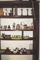 Shelf showing a variety of items including Wizard of Oz figurines, candlesticks, Cow Parade figure and natural stones