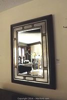 Full view of the vintage wall mirror mounted on a wall showing its rectangular shape, central mirror panel, beveled glass edging, and dark wooden frame.
