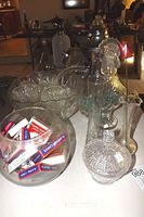 Full view of lot items including seltzer bottle, punch bowl set, glass rooster bottle, glass containers, and playing cards in clear bowl.