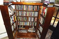 Wooden cabinet displaying a large collection of CDs and VHS tapes inside multiple shelves and doors.