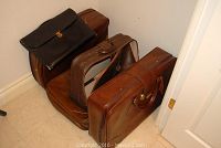 Four vintage luggage pieces arranged on floor: a leather suitcase, a soft-sided briefcase, and two soft-sided bags