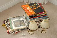 Stack of over 50 vinyl LP records in varied colorful covers with two small vintage table lamps with pleated cream shades and painted brass style bases placed beside the stack.