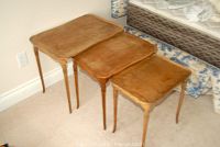 Overview of 3 wood nesting tables stacked inside each other showing scalloped edges and tapering legs.