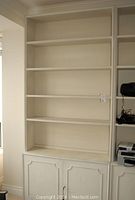 Front view of tall white painted wood bookcase with open shelves and bottom cabinet.