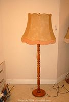 Full view of 62 inch tall standing lamp with turned wood base and beige fabric lampshade with fringe.