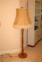 Full view of the standing lamp showing wooden base and beige shade with fringe.