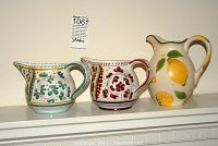 Three ceramic pitchers placed on a shelf showing two matching small pitchers and one larger lemon-themed pitcher.