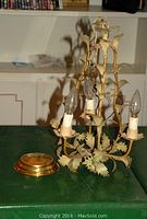 Front view of vintage metal wall sconce with three candle-style bulbs surrounded by leaf-shaped metal accents, showing the detached brass mounting plate.