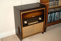 Front left angle view of vintage Grundig floor radio showing wooden cabinet, tuning display, and woven speaker grille.