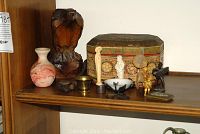 Photo of shelf with painted jewelry box, carved wooden eagle, marbled ceramic vase, brass mortar, and various small religious and decorative figurines.