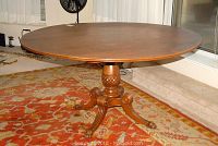 Full view of the round wooden antique table showing claw feet and pineapple pedestal base on an ornate carpet.