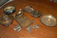 Overview of all silver-plated serving pieces on table: tureen, bowl, tray, chafing dish, trivet, rack and knife rests.