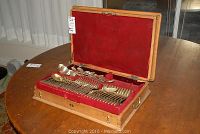 Open wooden chest showing red velvet-lined fitted tray with multiple silver flatware pieces