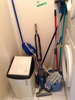 Photo showing white laundry hamper with black lid, Shark vacuum, mop, broom inside laundry area