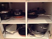 Cookware stored inside cabinet including frying pans, stock pots, and copper pans