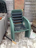 Stack of multiple green outdoor chairs with armrests arranged one on top of another, showing their stackable design.