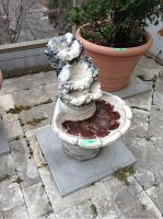 Three-quarter front view of the three-tiered leaf and bird concrete fountain showing water basin and base crack.