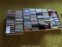 Large collection of CDs arranged in several rows and boxes on a carpeted floor.