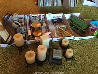 Assorted pillar candles, metal candle holders, glass decor items arranged on carpet