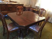 Dining table and five chairs in a room with patterned carpet and curtains, showing overall set from an angle.