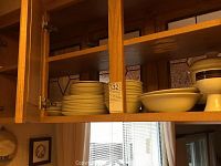 Shows stacked dinner plates, side plates, and bowls stored in wooden kitchen cabinets.