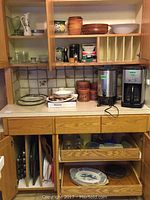 Various kitchenware items arranged on countertop and cabinet including Myott and Sons platters, wood bowls, glassware, plates, and coffee makers.