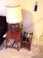 Photo of ceramic based lamp on wooden side table next to wooden magazine rack