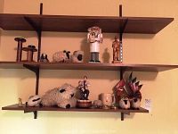 Shelf display of various decorative items including wooden sheep, farmer figure, brass magnifying glass, rooster figurine and small carved figures