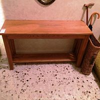 Full view of wooden entranceway or sofa table beside wicker umbrella stand and cane.